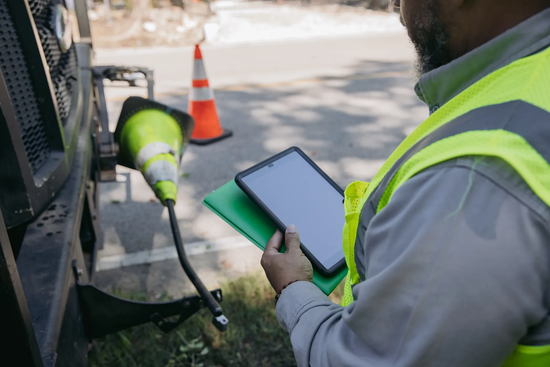 A crew leader in a safety vest holding a tablet beside a work truck and traffic cones